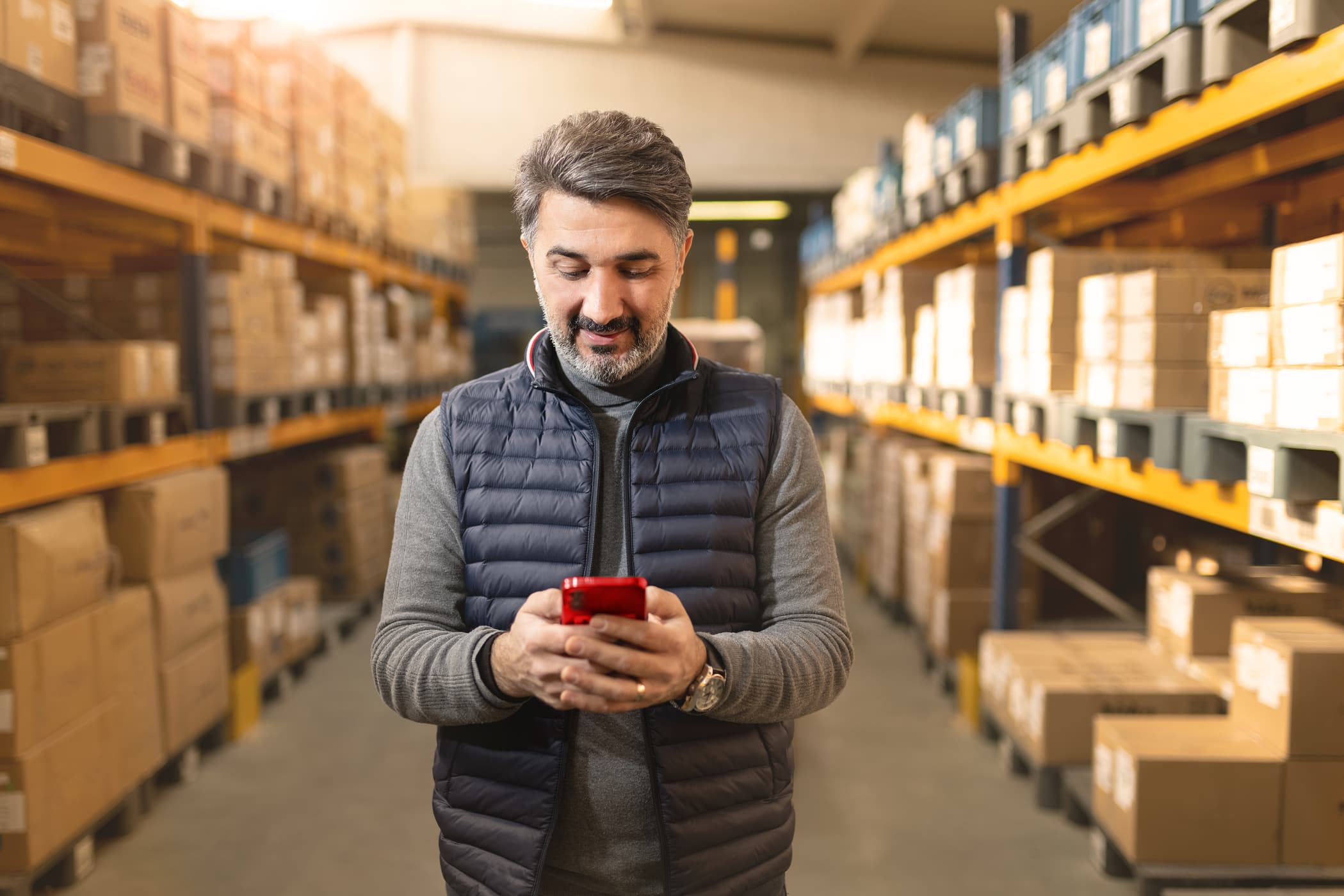 Mann mit Handy in der Hand zwischen Lagergestellen