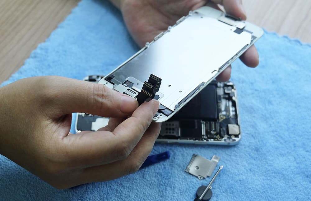 Jemand repariert ein iPhone. Es liegt zusammen mit dem Werkzeug auf dem Tisch.