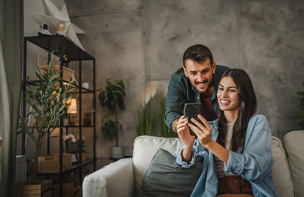 Zwei Erwachsene im Wohnzimmer schauen auf ein Smartphone