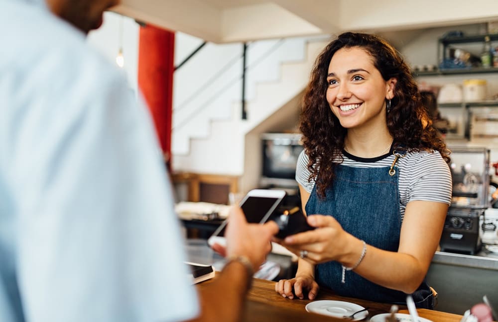 Mann bezahlt in Café mit Handy bei einer lachenden Frau 