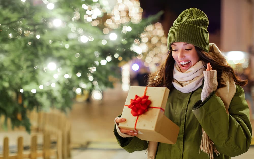 Une femme tient un cadeau dans ses bras et est super contente.