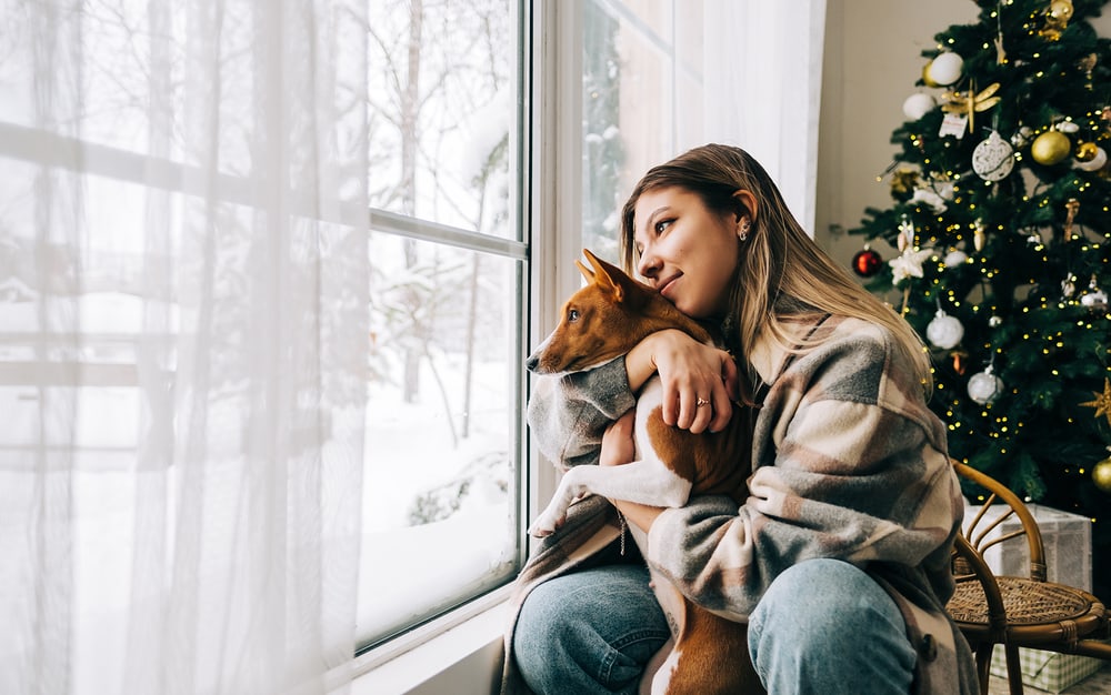 Una donna è seduta con il suo cane davanti all'albero di Natale, senza dispositivi mobili.
